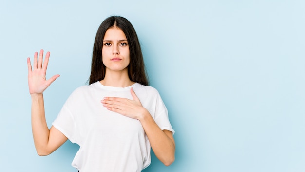 Giovane donna caucasica sulla parete blu facendo un giuramento, mettendo la mano sul petto.