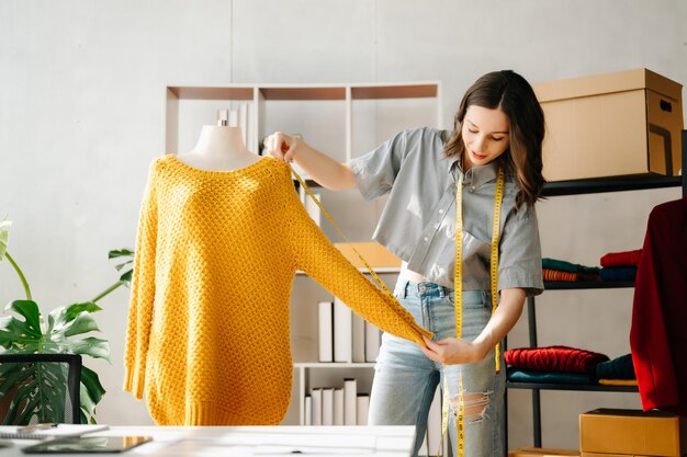 Giovane donna caucasica sulla scrivania dell'ufficio di casa di un designer di moda e tiene in mano un tablet, un portatile e uno smartphone