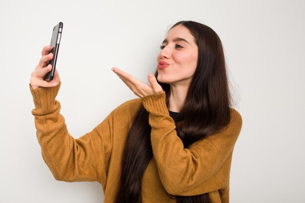 Giovane donna caucasica tramite telefono cellulare isolato su sfondo bianco