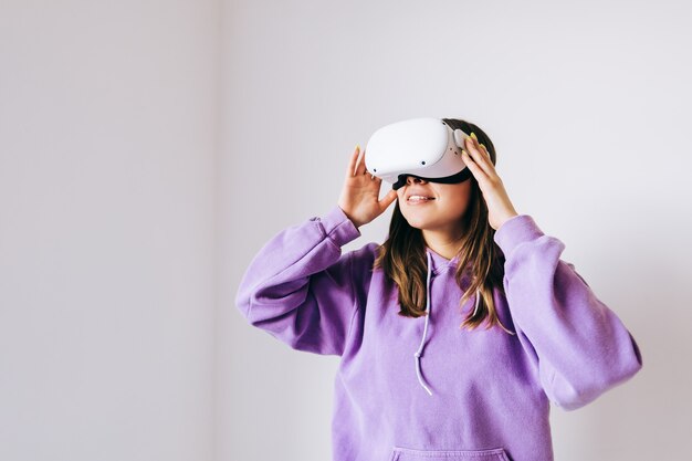 Giovane donna caucasica utilizzando auricolare Vr, toccando gli occhiali e alzando lo sguardo nella realtà virtuale su sfondo bianco.