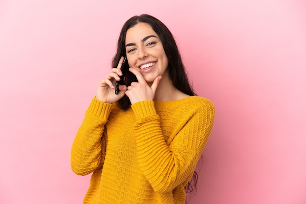 Giovane donna caucasica utilizzando il telefono cellulare isolato sulla parete rosa felice e sorridente