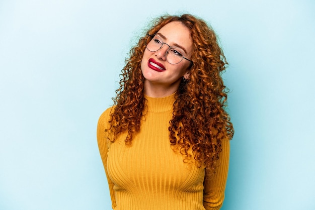 Giovane donna caucasica zenzero isolata su sfondo blu collo ridente rilassato e felice allungato che mostra i denti