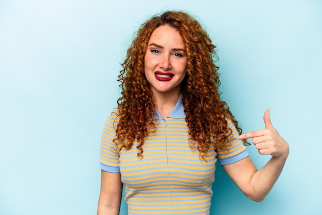 Giovane donna caucasica zenzero isolata su sfondo blu persona che punta a mano a uno spazio di copia camicia orgoglioso e fiducioso