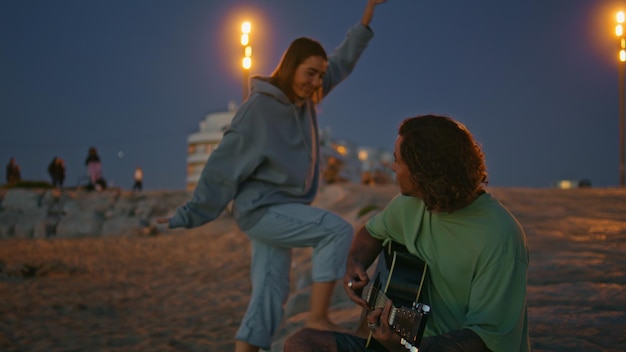 Giovane donna che abbraccia il fidanzato alla sera sulla spiaggia sabbiosa uomo che suona la chitarra