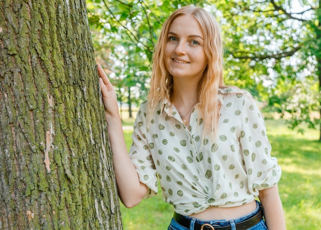 Giovane donna che abbraccia un grande albero in una giornata estiva. Ecofriendly o concetto di natura