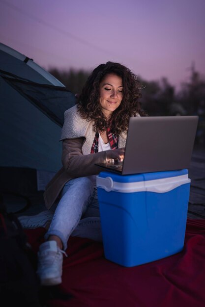 Giovane donna che accampa vicino al lago seduta all'ingresso della tenda e che lavora