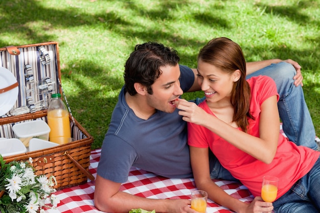 Giovane donna che alimenta il suo amico come loro si trovano su una coperta con un picnic