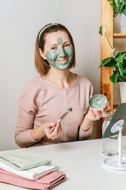 Giovane donna che applica una maschera di argilla blu per il viso facendo procedure termali Concetto di cura della pelle del viso