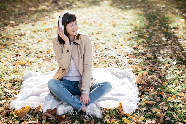 Giovane donna che ascolta la musica con le cuffie nella foresta di autunno