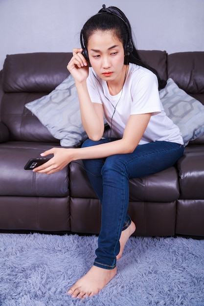 giovane donna che ascolta la musica in cuffia con moblie sul divano a casa