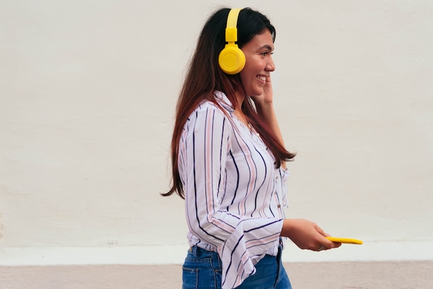 Giovane donna che ascolta la musica sul telefono cellulare contro il muro