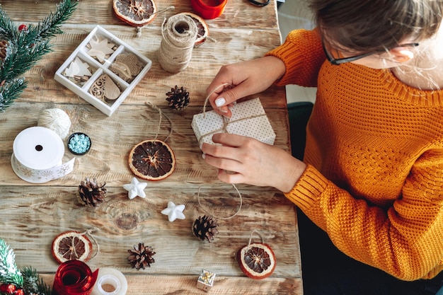 Giovane donna che avvolge il regalo di Natale sul tavolo con decorazioni di capodanno