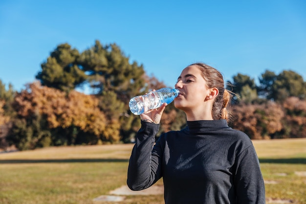 Giovane donna che beve acqua da bottiglia in un parco pubblico