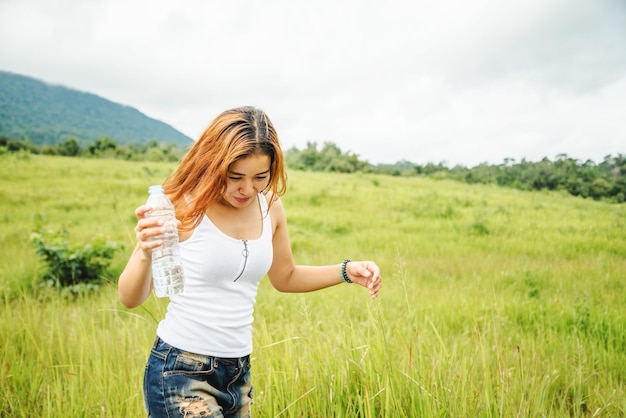 Giovane donna che beve acqua sul campo contro il cielo