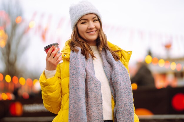 Giovane donna che beve caffè caldo mentre si cammina vicino all'albero di Capodanno.