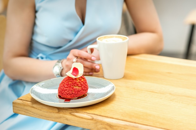 Giovane donna che beve caffè con una fetta di torta seduta al tavolo in un bar all'aperto