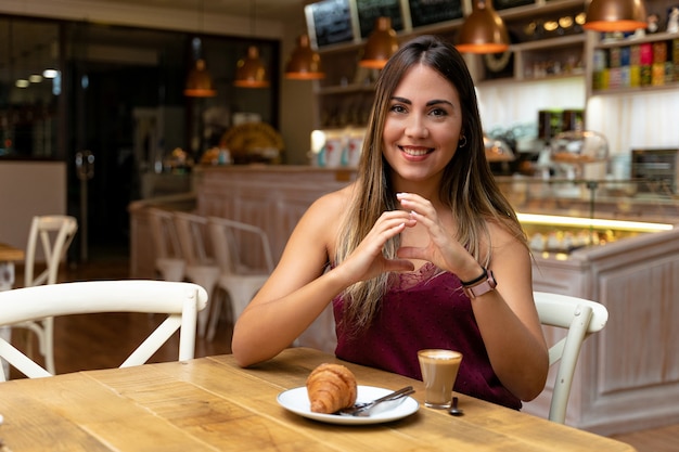 Giovane donna che beve caffè e che fa il segno della comunicazione