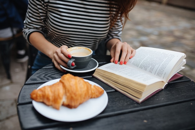 giovane donna che beve caffè e legge un libro sulla terrazza del bar