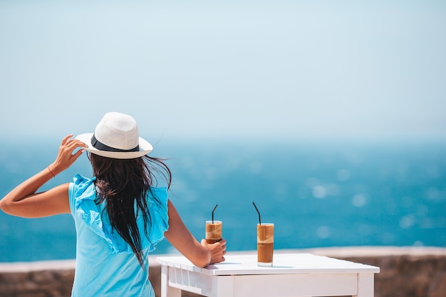 Giovane donna che beve caffè freddo godendo della vista sul mare nella caffetteria all'aperto