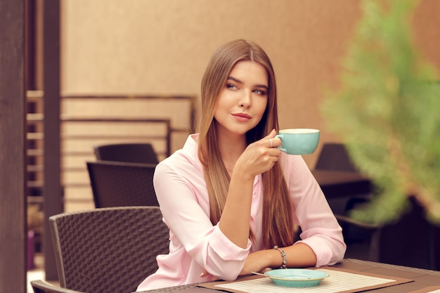 Giovane donna che beve caffè in un bar all'aperto