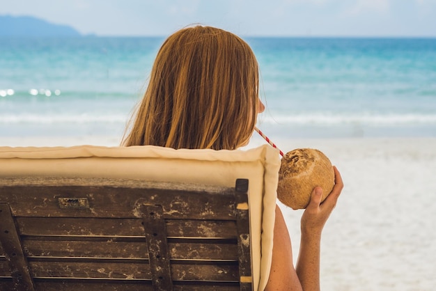 Giovane donna che beve latte di cocco su Chaise-longue sulla spiaggia.