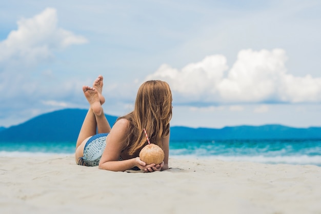 Giovane donna che beve latte di cocco sulla spiaggia