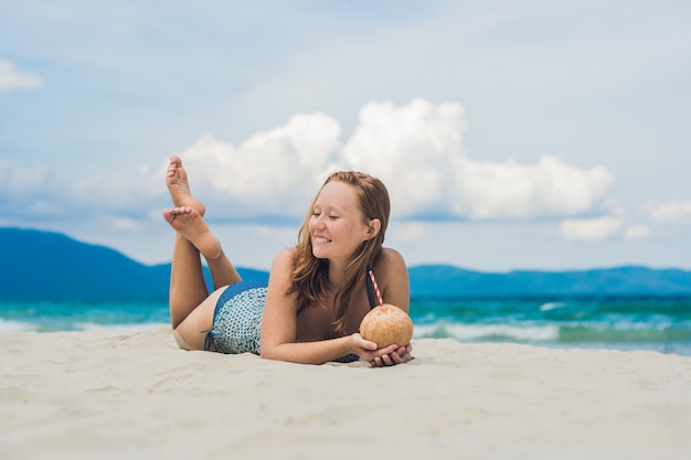 Giovane donna che beve latte di cocco sulla spiaggia