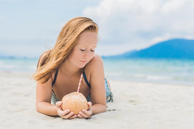 Giovane donna che beve latte di cocco sulla spiaggia.