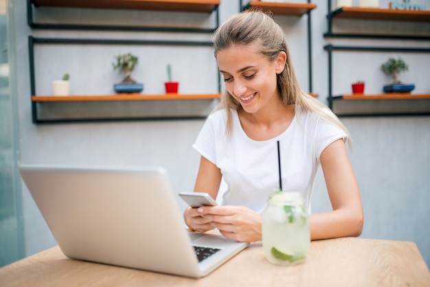 Giovane donna che beve limonata e navigare sul web. Utilizzando telefono e laptop.