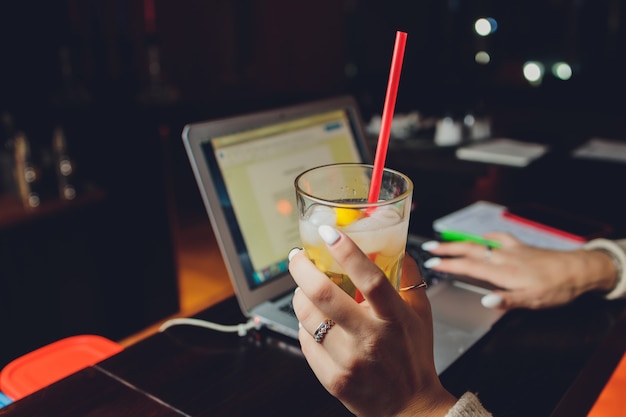 Giovane donna che beve limonata fresca mentre si lavora al computer portatile nella caffetteria, primo piano.