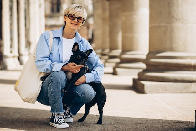 Giovane donna che cammina in città con il suo bulldog francese dell'animale domestico