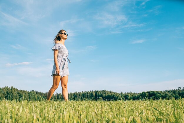 Giovane donna che cammina nel campo soleggiato verde