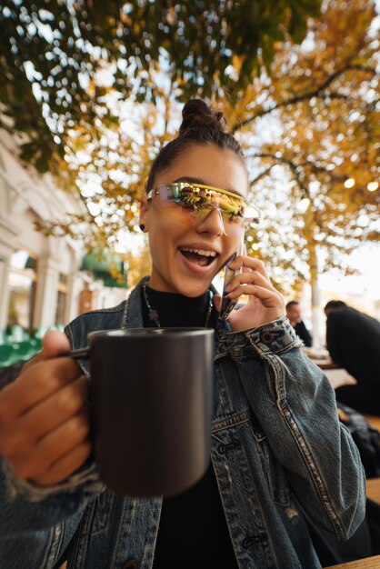 Giovane donna che chiama smartphone e beve bevande al caffè di strada