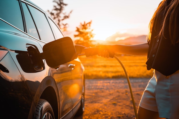 Giovane donna che collega il caricabatterie in un concetto di energia rinnovabile di un'auto elettrica nera