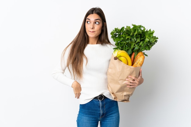 Giovane donna che compra del cibo isolato sul muro bianco avendo dubbi e pensando