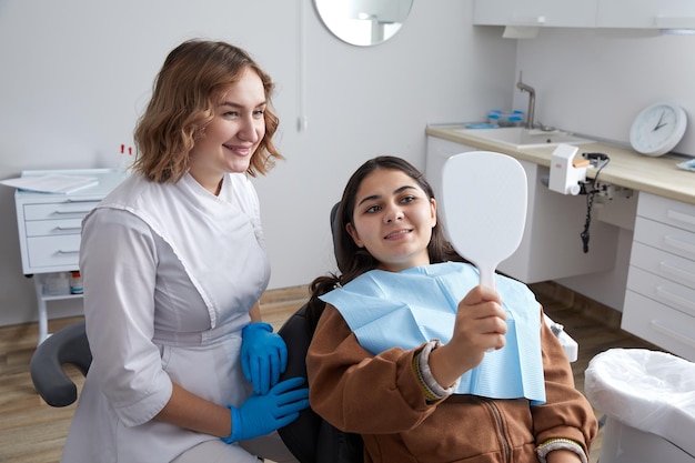 Giovane donna che controlla il suo bellissimo sorriso nello specchio dopo un trattamento stomatologico