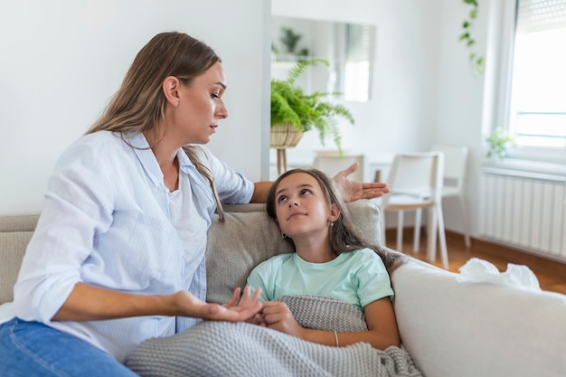 Giovane donna che controlla la temperatura con la mano della piccola figlia malata. Madre che controlla la temperatura della sua ragazza malata. Bambino malato sdraiato sul letto sotto la coperta con la donna che controlla la febbre sulla fronte a mano.