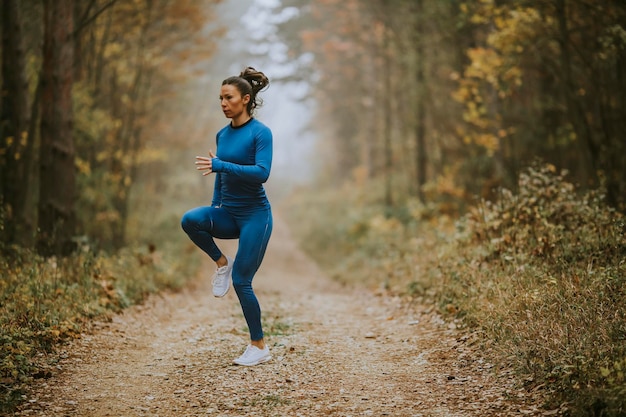 Giovane donna che corre facendo esercizio sul sentiero nel bosco in autunno