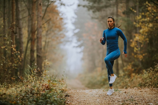 Giovane donna che corre facendo esercizio sul sentiero nel bosco in autunno
