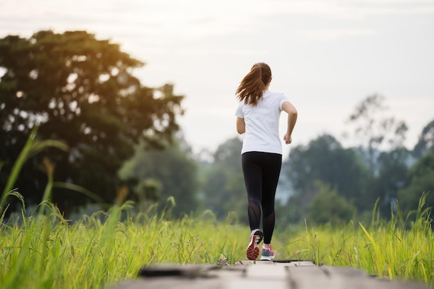 Giovane donna che corre sul sentiero di legno nel campo