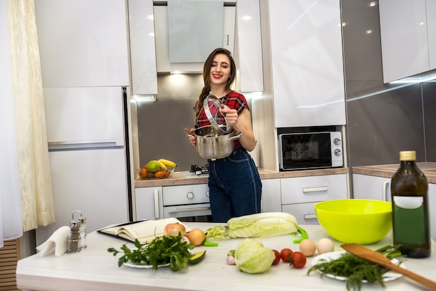 Giovane donna che cucina il cibo in una pentola in cucina.