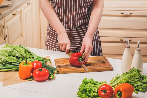 Giovane donna che cucina in cucina a casa. Cibo salutare. Dieta. Concetto di dieta. Uno stile di vita sano. Cucinare a casa. Prepara da mangiare. Una donna taglia un peperone e delle verdure con un coltello.