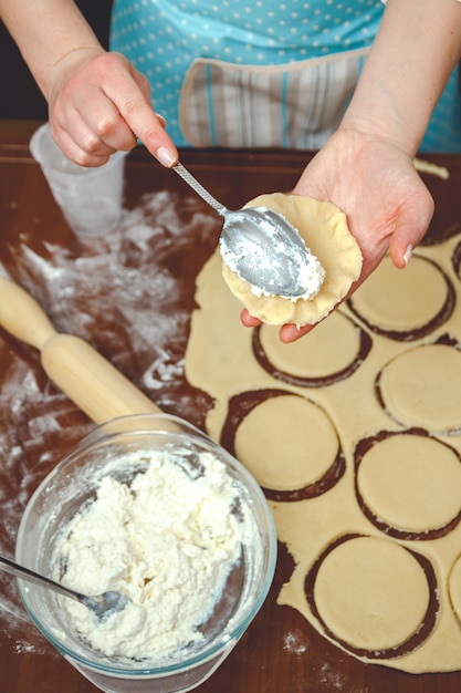 Giovane donna che cucina in cucina, prepara l'impasto per la cottura, aggiunge un ripieno di ricotta nella torta