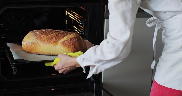 Giovane donna che cuoce pane fresco fatto in casa nel forno Fare il pane in casa Cottura del pane