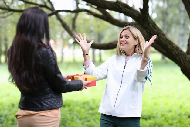 Giovane donna che dà alla sua amica la scatola con un regalo nel parco buon compleanno concept