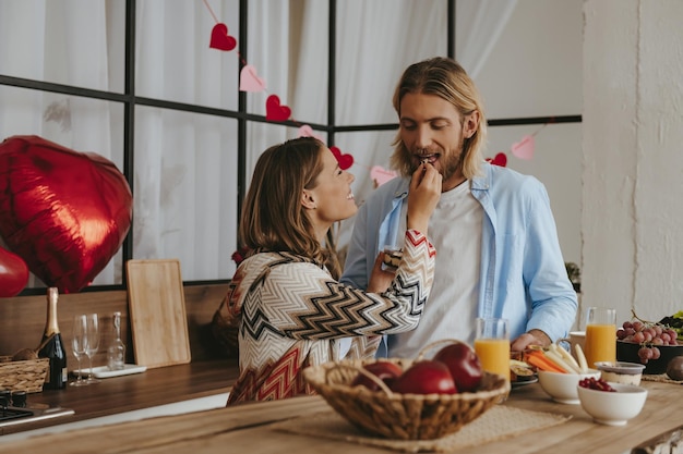 Giovane donna che dà da mangiare al suo ragazzo con la colazione mentre si gusta cibo sano in cucina insieme