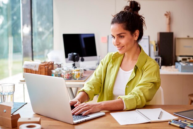 Giovane donna che esegue attività online da casa vendendo candele boutique utilizzando il computer portatile