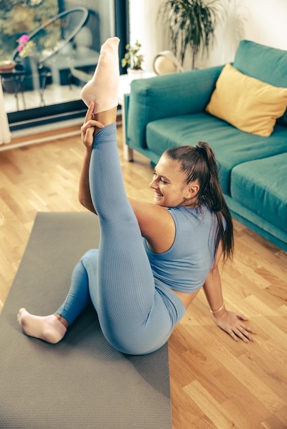 Giovane donna che esercita ginnastica a casa al mattino. Sta facendo un allenamento di stretching sul tappetino per esercizi.