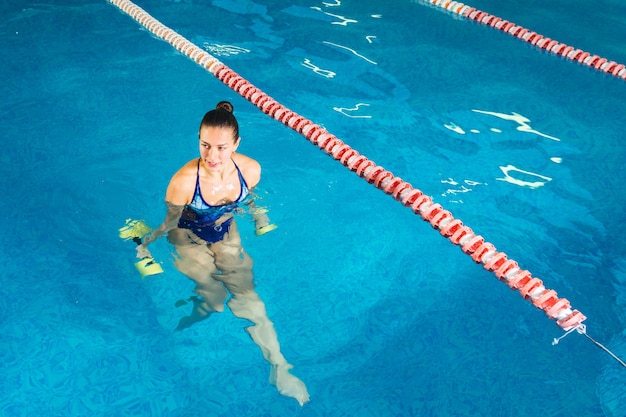 Giovane donna che fa aerobica in acqua in piscina coperta, concetto sportivo