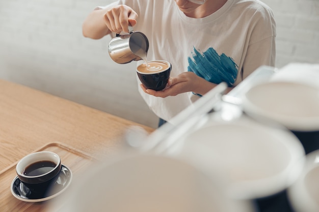 Giovane donna che fa arte del latte in caffetteria